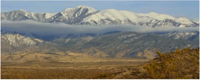 Snow-covered mountains rising above a wooded foothill landscape.