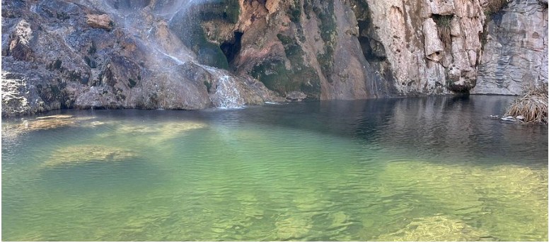 A clear pool below a rocky canyon wall.